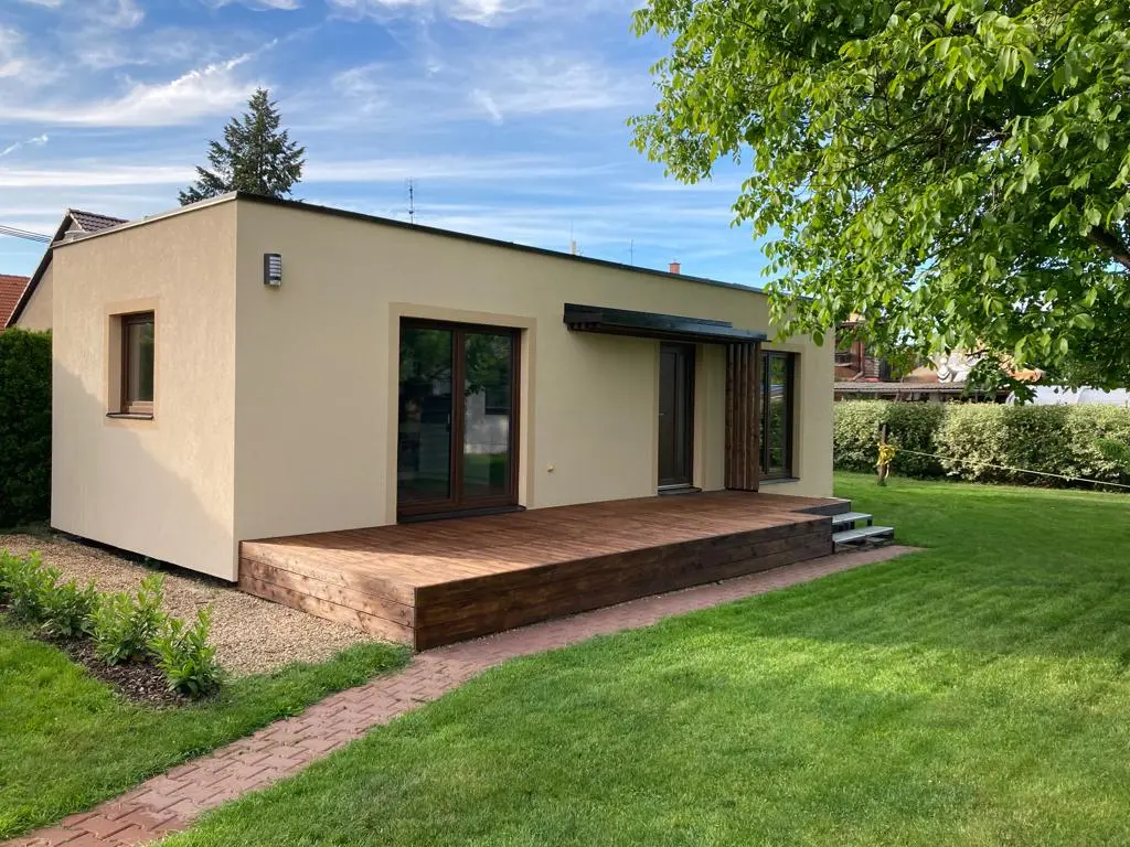 Modulový bungalov Pardubice se světlou omítkou, dřevěnou terasou se schody a oplocenou zahradou
