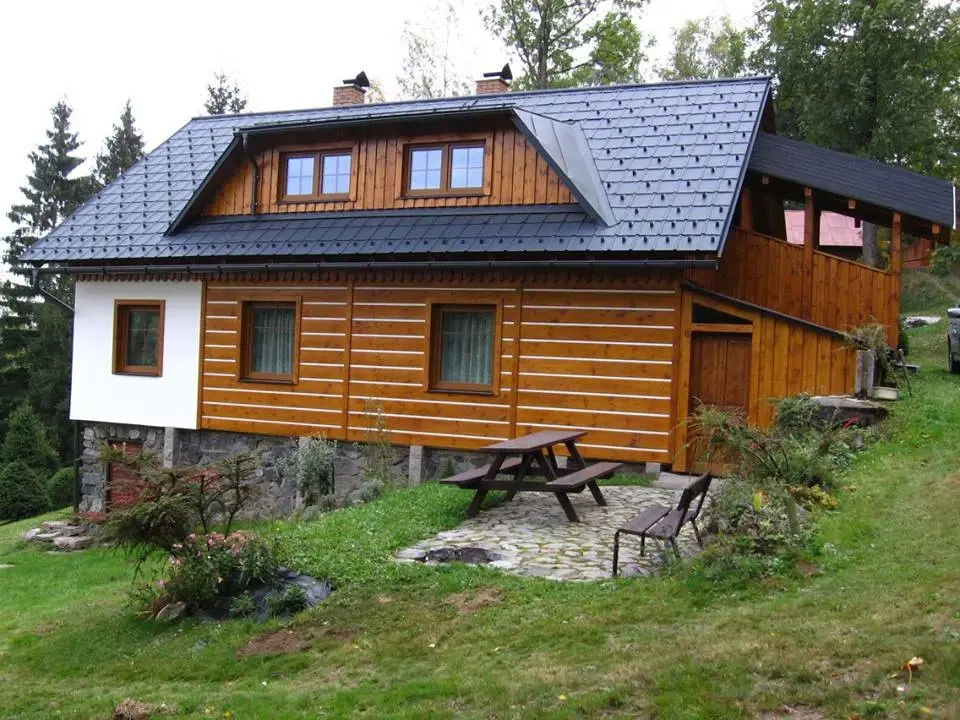 Dokončená horská roubenka Deštné s dřevěným obkladem, antracitovou střechou a venkovním posezením