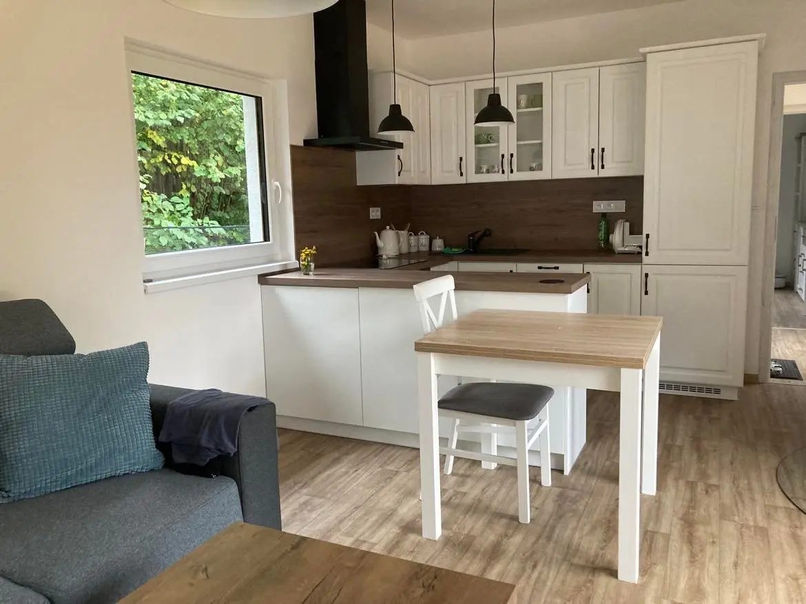 Bílá kuchyňská linka s barovou deskou a malým jídelním stolem v modulovém bungalovu Solnice
