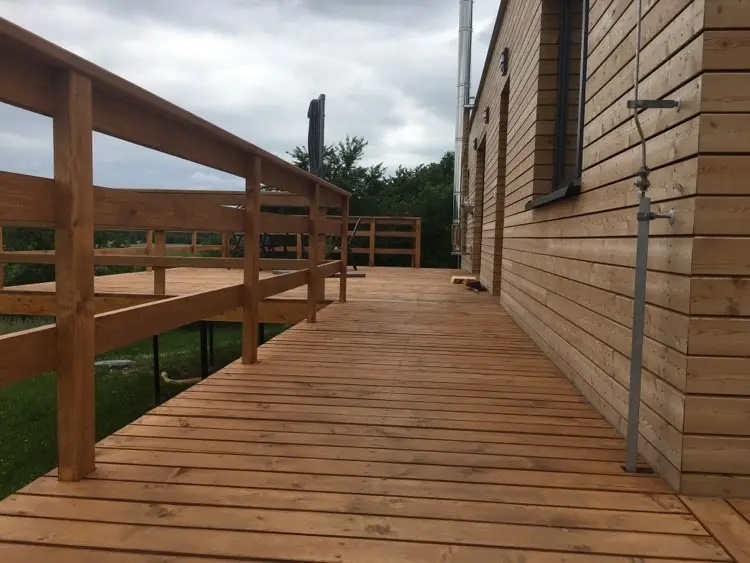 Dřevěná terasa s dřevěným zábradlím podél boku modulového bungalovu Synkov